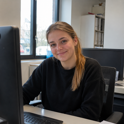 Portraitfoto einer Frau am Schreibtisch im Büro, lächelnd in die Kamera blickend
